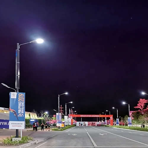 A night view of a street with illuminated poles, banners, and a red gateway leading to a venue.