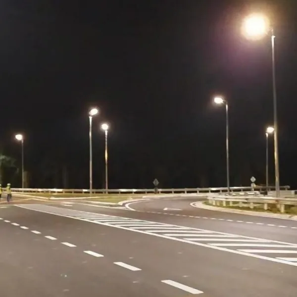 A quiet, empty curved road at night illuminated by several tall streetlights.